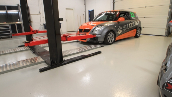 Bilværksted med epoxy gulv i lysegrå udført af PerBro Gulve i Kolding. Suzuki racerbil på løfteplatform.
