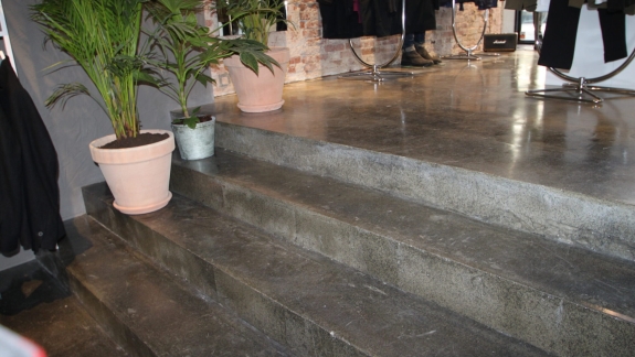 Epoxy gulv og trappe i butiksmiljø fra PerBro Gulve i Kolding. Råt look med grønne planter og rå murstensvæg.