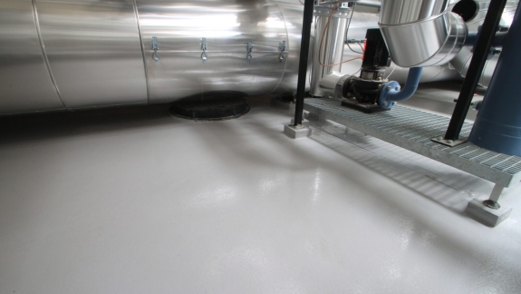 Detaljebillede af epoxy gulv i fabrikshal, udført af PerBro Gulve i Kolding. Rørføring og pumper skaber teknisk miljø.