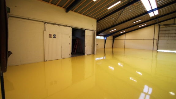 Gul epoxy gulv i stor lagerhal, installeret af PerBro Gulve i Kolding. Blank finish og god belysning.